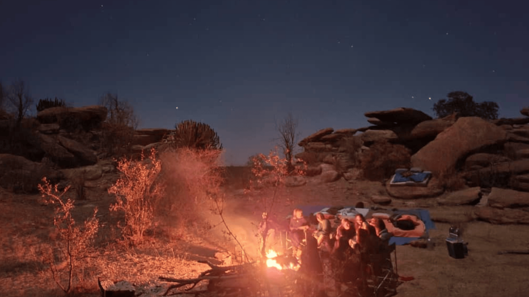 A group of teen volunteers gather around the campfire under the stars